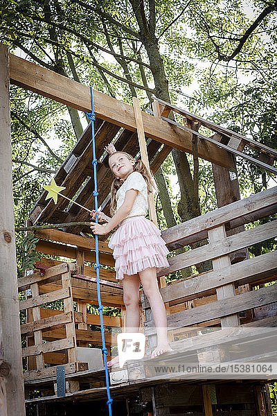 Girl dressed as a princess with crown and sceptre playing in a tree house