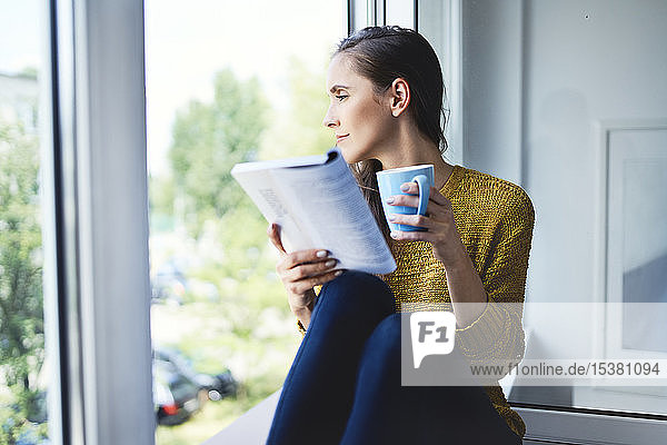 Young woman looking out the window while reading book at home