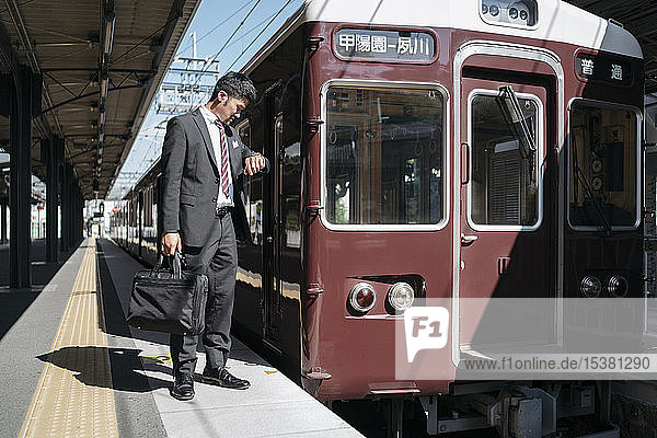 Junger Geschäftsmann auf einem Bahnsteig der die Zeit überprüft