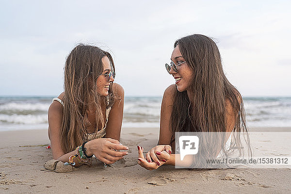 Zwei glückliche Freundinnen liegen am Strand und unterhalten sich