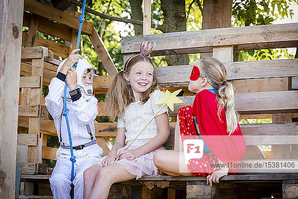 Drei Kinder mit Superhelden-Kostümen spielen auf ihrem Baumhaus