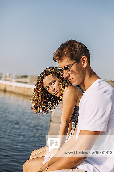 Junges Paar sitzt auf einer Mole am Meer
