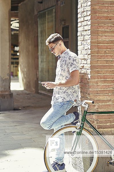 Mann mit Fahrrad  der sich mit seinem Smartphone an eine Wand lehnt