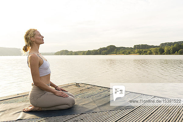 Junge Frau  die auf einem Steg an einem See Yoga praktiziert