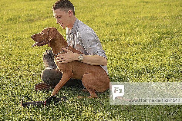 junger Mann mit seinem Hund  kuschelnd auf einer Wiese