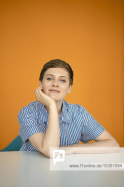 Porträt einer auf Tisch gelehnten Frau mit orangem Hintergrund