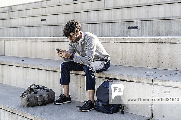 Mann sitzt auf einer Außentreppe und benutzt ein Smartphone