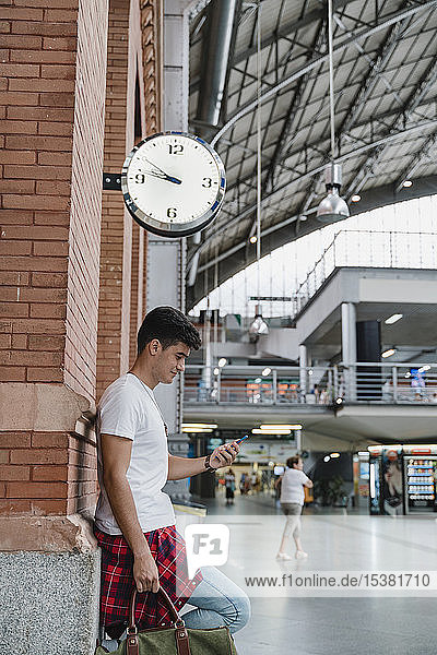 Junger Mann wartet am Bahnhof mit Smartphone
