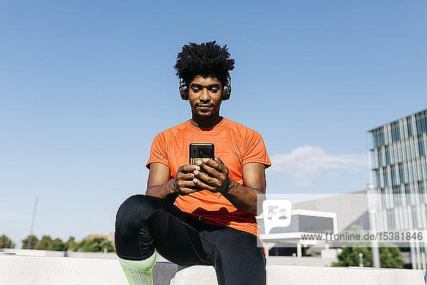 Junger Sportler sitzt auf einer Treppe  benutzt ein Smartphone und hört Musik