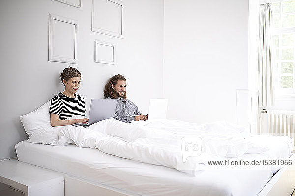 Junges Paar benutzt zu Hause Laptops im Bett