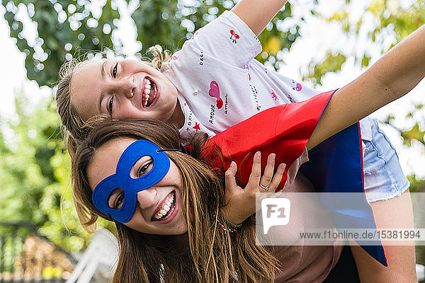 Zwei glückliche Schwestern mit Augenmaske spielen im Garten