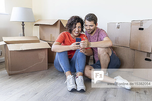 Glückliches Paar benutzt Handy im neuen Zuhause