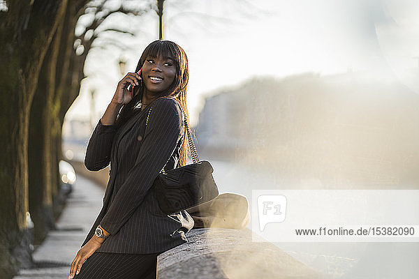 Smiling businesswoman standing at rivershore using her smartphone