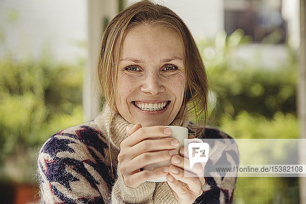 Porträt einer lächelnden jungen Frau  die einen flauschigen Pullover trägt und eine Tasse hält