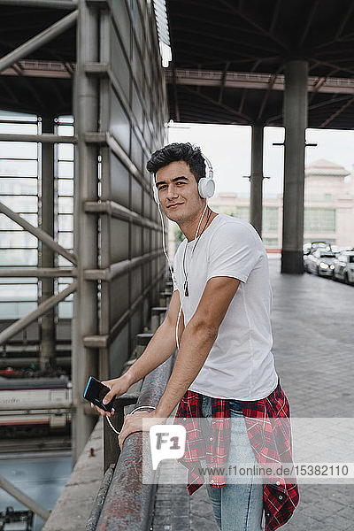 Young man waiting at train station with smartphone and wearing headphones