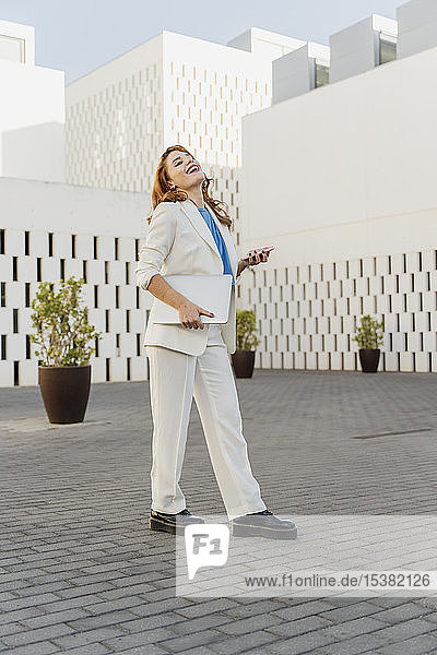 Geschäftsfrau in weißem Hosenanzug  mit Laptop  mit Smartphone