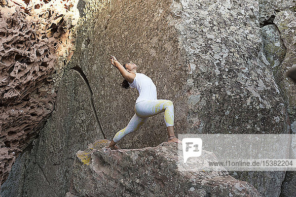 Junge Asiatin praktiziert Yoga auf einem Felsen  Krieger-Pose