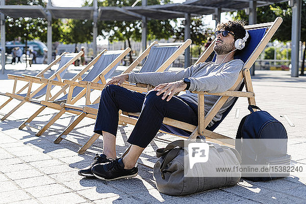 Mann entspannt sich im Liegestuhl auf städtischem Platz und hört Musik