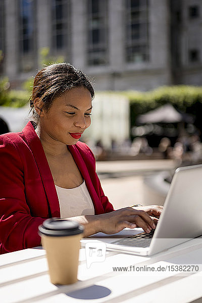 Porträt einer lächelnden Geschäftsfrau  die im Freien am Laptop arbeitet  London  UK