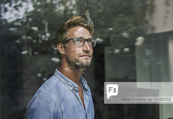 Casual young businessman behind windowpane in office