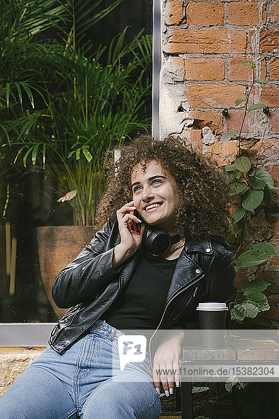 Portrait of happy teenage girl on the phone sitting at outdoor cafe with coffee to go