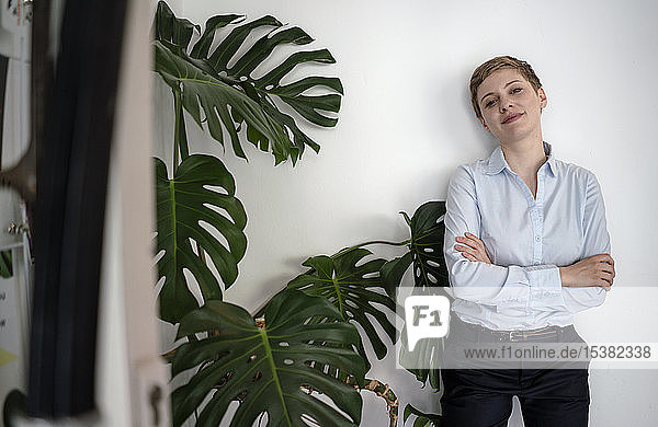 Porträt einer selbstbewussten Geschäftsfrau  die an einer Wand neben einer Pflanze steht