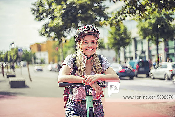 Porträt einer entspannten jungen Frau mit Fahrradhelm  die am Lenker eines E-Scooters lehnt  Berlin  Deutschland