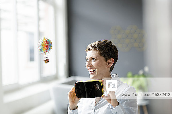 Lächelnde Frau mit VR-Brille und kleinem Heißluftballon im Büro