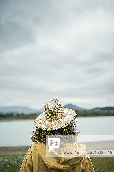 Rückansicht einer jungen Frau mit Strohhut  die auf einen See schaut