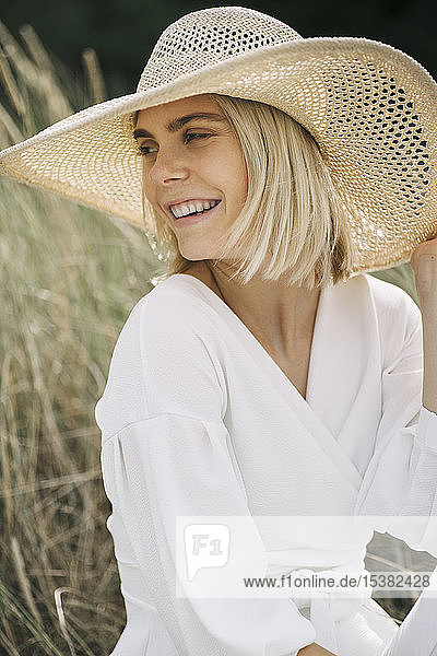 Portrait of blond young woman in dunes wearing white wrap blouse and summer hat