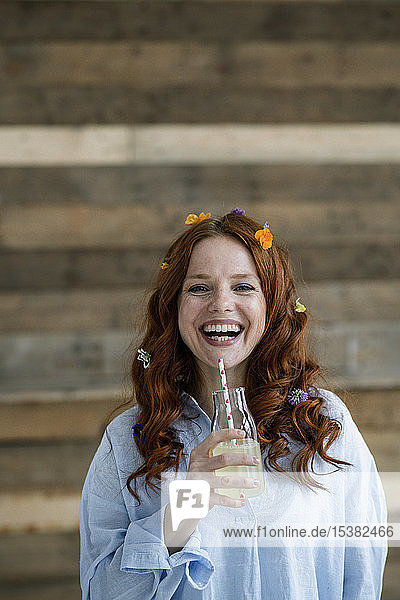 Porträt einer lachenden rothaarigen Frau mit Blüten im Haar  die Limonade trinkt