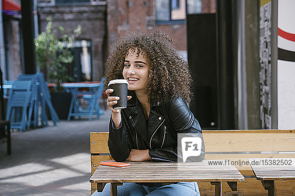 Porträt eines lächelnden Teenagers  der auf einer Bank sitzt und Kaffee zum Mitnehmen trinkt