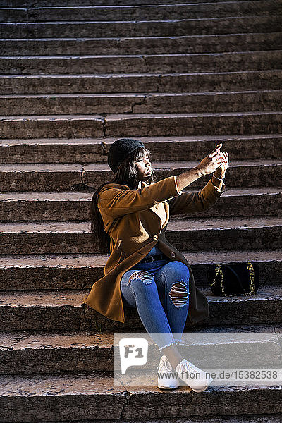 Touristin  die auf einer Treppe sitzt und im Freien ein Selfie macht