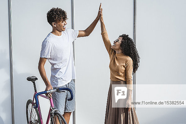 Glückliches Paar mit Fahrrad vor weißem Zaun stehend  High-Five