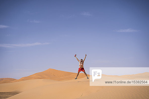 Übergewichtiger Mann mit Schwimmshorts springt in der Wüste von Marokko