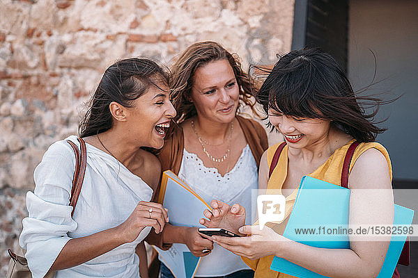 Drei glückliche Freundinnen mit Smartphone im Freien