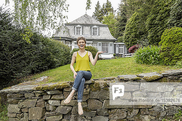 Glückliche Frau sitzt auf einer Mauer im Garten