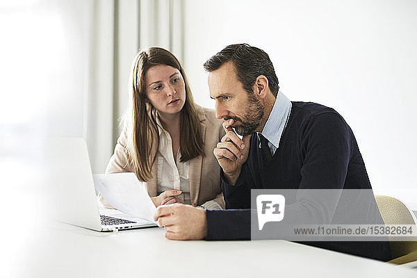 Businessman and employee with laptop and documents working at desk in office