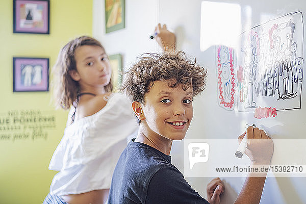 Portrait of smiling boy drawing on a whiteboard with girl in background