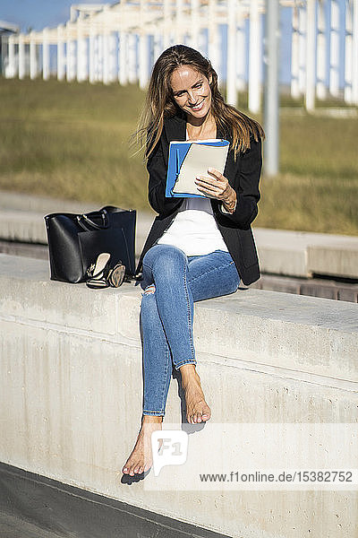 Lächelnde Geschäftsfrau sitzt mit einem Notizbuch an einer Wand