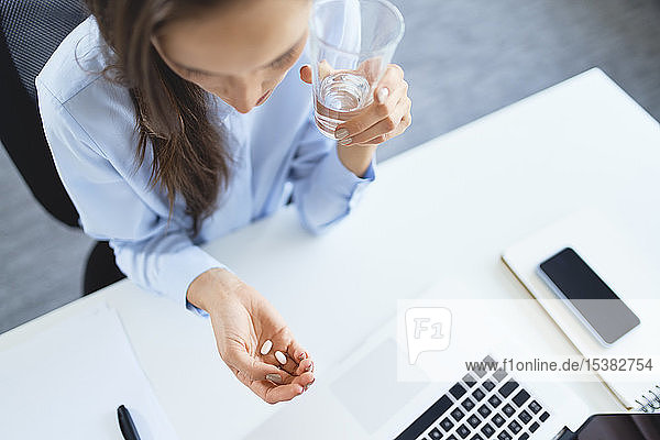 Overhead view of woman taking painkillers while sitting on office