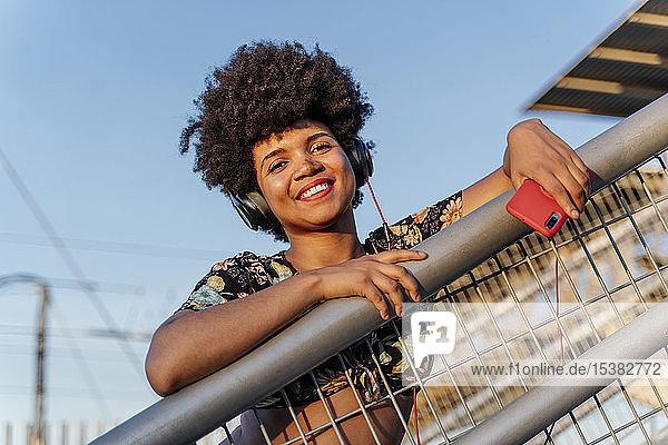 Lächelnde afro-amerikanische Frau mit rotem Smartphone und Kopfhörern