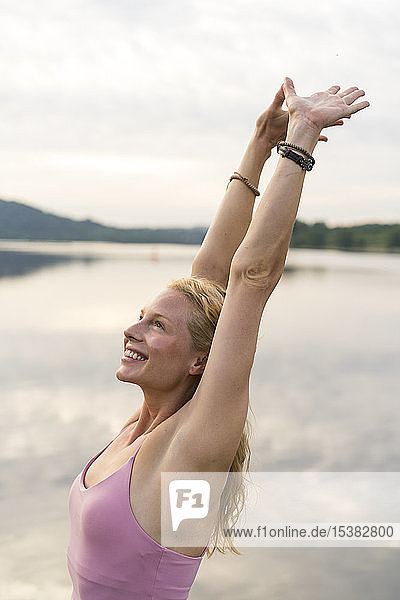 Glückliche junge Frau hebt ihre Arme an einem See