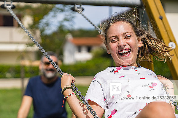Porträt eines glücklichen Mädchens auf einer Schaukel mit dem Vater im Hintergrund