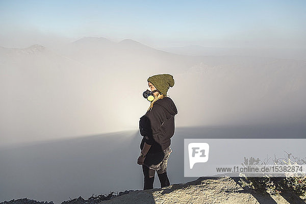 Junge Frau mit Atemschutzmaske steht am Rande des Vulkans Ijen  Java  Indonesien