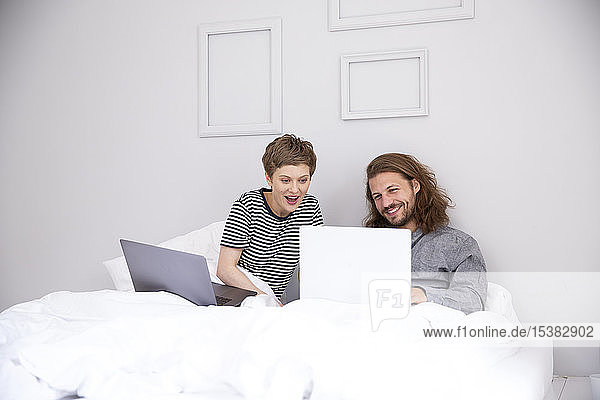 Junges Paar mit Laptops im Bett zu Hause