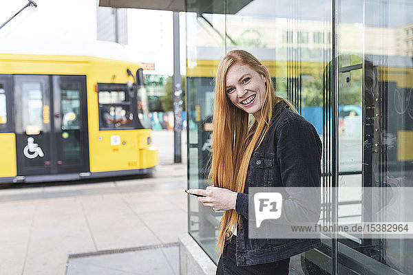 Porträt einer rothaarigen jungen Frau mit Smartphone in der Stadt  Berlin  Deutschland
