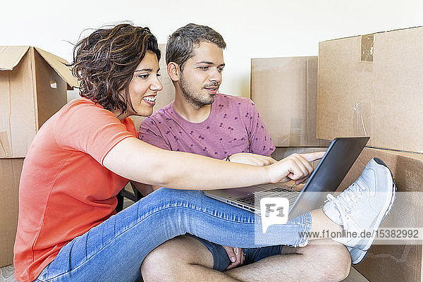 Happy couple moving into new home using laptop