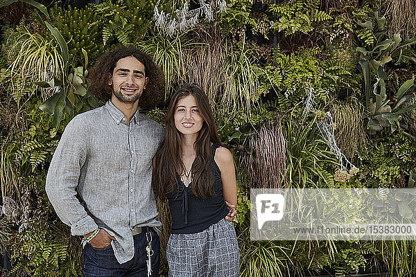 Portrait of smiling young couple in front of plant wall