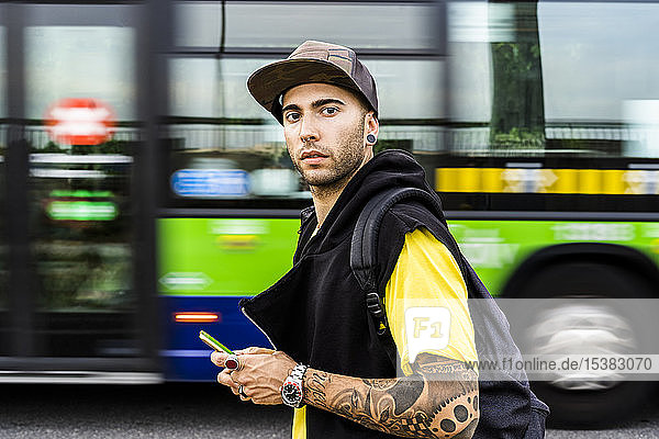 Porträt eines tätowierten jungen Mannes mit Smartphone in der Stadt